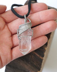 Clear quartz point pendant in hand for size reference – natural crystal, white gold copper wire, April birthstone, masculine design.