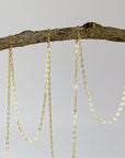 Gold chains hanging from a branch on a light gray background