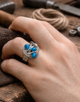 Hand wearing a silver ring with blue stones on a wooden surface with tools.