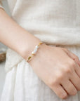Hand wearing a pearl bracelet on a neutral background