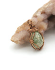 Copper-wrapped green stone pendant on a white background