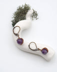 Bird’s eye view of amethyst drop earrings laying flat on a display, showing detailed wire wrapping and gemstone color.