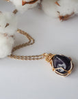 Detailed front view of women’s polished dark amethyst pendant on gold chain, artisan wire wrapped in gold plated copper