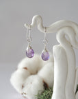 Detailed front view of handcrafted amethyst sterling silver drop earrings with natural faceted amethyst, artisan wire wrapping, hanging from a display – Designs by Nature Gems