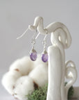 Side view of amethyst sterling silver drop earrings showing wire wrapped natural faceted amethyst, artisan craftsmanship, on a display – Designs by Nature Gems