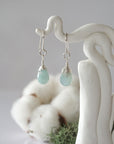 Detailed front view of handcrafted aquamarine sterling silver drop earrings with natural faceted aquamarine, artisan wire wrapping, hanging from a display – Designs by Nature Gems