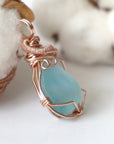 Side view of a blue topaz pendant showing the depth of the stone and its rose gold wire wrap