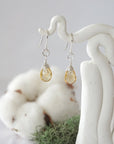 Detailed front view of handcrafted citrine sterling silver drop earrings with natural faceted citrine, artisan wire wrapping, hanging from a display – Designs by Nature Gems