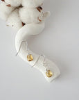 Citrine sterling silver drop earrings with faceted natural citrine stones and wire wrapping, laying flat on a display – Designs by Nature Gems