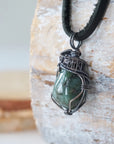 Left angle detail of emerald pendant for men showing natural polished-raw emerald and artisan antiqued sterling silver wire wrapping