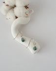 Emerald sterling silver drop earrings with faceted natural emerald stones and wire wrapping, laying flat on a display – Designs by Nature Gems