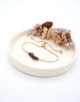 Handmade garnet bracelet displayed on ceramic tray showing natural red crystals and gold chain - January birthstone gift for her