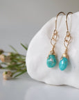 Left side angle of gold turquoise dangle earrings displaying handmade wire wrapped design and natural stone variation