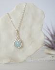 Zoomed in look at minimalist aquamarine necklace on display, artisan wire wrapped, soft silver finish, March birthstone