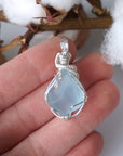 Natural blue topaz pendant hand wire-wrapped in sterling silver, held between fingers to show its size