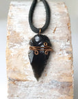 Detailed front view of men’s black obsidian arrowhead necklace on black leather cord, antique bronze copper wire wrap, by Designs by Nature Gems.