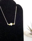 Focused left-side close-up of sterling silver peridot and pearl bar necklace on jewelry display