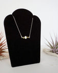 Right angle view of peridot and freshwater pearl bar necklace in 925 sterling silver on jewelry display