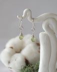 Detailed front view of handcrafted peridot sterling silver drop earrings with natural faceted peridot, artisan wire wrapping, hanging from a display – Designs by Nature Gems