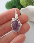 Raw amethyst crystal pendant wire wrapped in sterling silver held in hand showing size