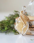 Close up of wire wrapped raw citrine crystal showing silver and gold plated copper craftsmanship and natural unpolished stone texture