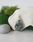 Back angle look at simple raw emerald pendant with silver wire wrapping