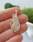 Handmade raw Ethiopian opal pendant held in hand showing size — natural opal stone wire wrapped in 925 sterling silver, 7-10 carats, one of a kind