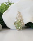 Detailed front angle view of simple raw peridot pendant in silver wire
