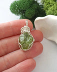 Handmade raw peridot pendant held in hand showing size — natural green peridot stone wire wrapped in 925 sterling silver, approx. 1 inch, one of a kind