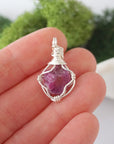 Simple raw pink ruby pendant shown in hand for size reference