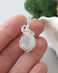 Raw rainbow moonstone crystal pendant wire wrapped in sterling silver held in hand showing size