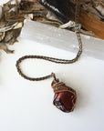 Natural red tiger's eye pendant on antique bronze chain, laying flat, artisan jewelry by Designs by Nature Gems.