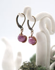 Side angle of ruby drop earrings on a display stand, highlighting antique bronze copper wire wrapping.