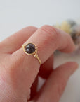 Simple garnet ring with polished garnet bead in minimalist gold wire wrap on woman’s hand