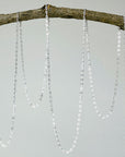 Silver chain necklaces hanging from a branch on a white background