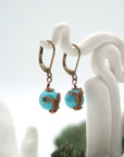 Side angle of turquoise drop earrings on a display stand, highlighting antique bronze copper wire wrapping.
