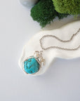 Handmade silver wire wrapped turquoise and freshwater pearl necklace laying flat on a silver plated chain, artisan jewelry for women