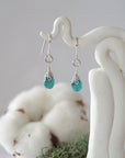 Detailed front view of handcrafted turquoise sterling silver drop earrings with natural faceted turquoise, artisan wire wrapping, hanging from a display – Designs by Nature Gems