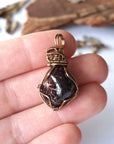 Women’s garnet pendant necklace in antique bronze copper held in hand for size reference, featuring a natural deep red garnet stone