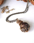 Women’s garnet wire wrapped necklace in antique bronze copper on an antique bronze chain, shown laying flat to highlight the natural garnet pendant