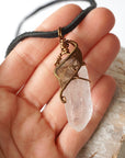 Clear quartz point pendant in hand for size reference – natural crystal, antique bronze copper wire, April birthstone, masculine design.
