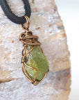 Right angle close-up of men's peridot necklace – detailed bronze copper wire wrapping, raw peridot, black leather cord.