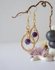 Side view of wire wrapped amethyst dangle earrings in gold plated copper with fish hook ear wires and teardrop frame