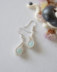 Aquamarine drop earring laying flat, displaying full pendant and fish hook, soft silver finish