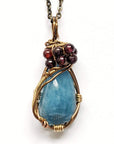 Angled view of a wire wrapped aquamarine pendant necklace with garnet accent beads on an antique bronze chain