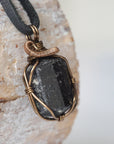 Right side angle detail of raw black tourmaline necklace on black leather cord, wire wrapped pendant by Designs by Nature Gems.