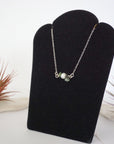Left angle view of emerald and pearl bar necklace in 925 sterling silver on jewelry display