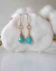 Gold turquoise drop earrings with wire wrapped crystal beads hanging on display, front view showing detailed craftsmanship