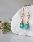 Left side angle of gold turquoise dangle earrings displaying handmade wire wrapped design and natural stone variation