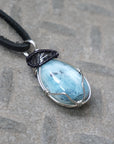Men's aquamarine pendant on a black leather cord, detailed side angle view with artisan wire wrapping in black and white gold finish, Designs by Nature Gems